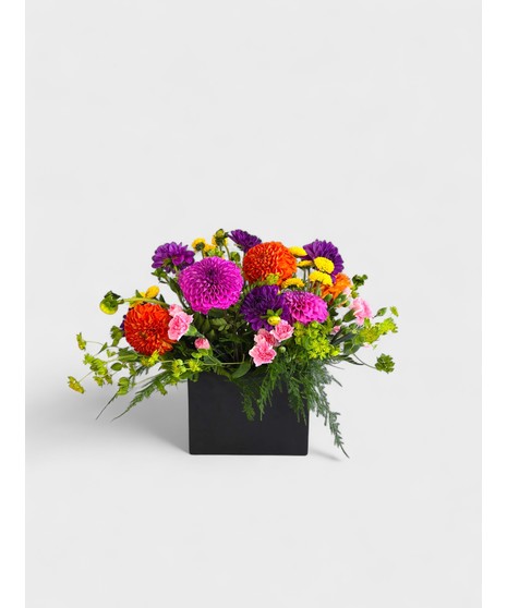 Mix of dahlias and fresh greenery in a modern coral glass vase