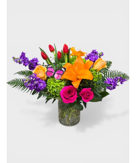 Bright and beautiful fresh flowers designed in a clear cylinder vase. Orange, pinks, and purples blended with green Hydrangea and a little butterfly kiss! 