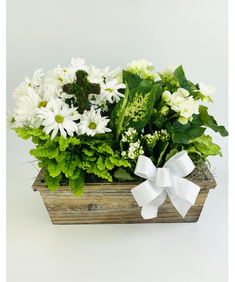 A serene garden of classic white blooming and tropical green plants with a moss and twig cross as the focal piece.