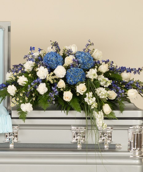 Blue and white casket spray features a mix of roses, delphinium, hydrangea and other accenting flowers. 