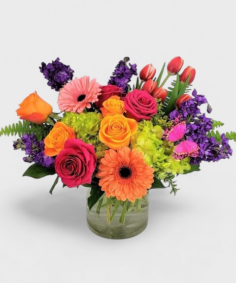 Bright and beautiful fresh flowers designed in a clear cylinder vase. Orange, pinks, and purples blended with green Hydrangea and a little butterfly kiss! 
