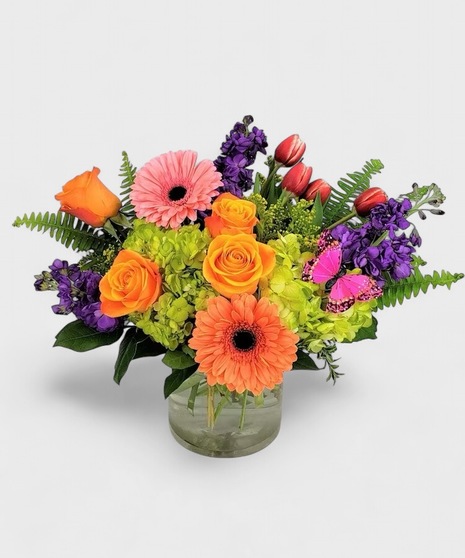 Bright and beautiful fresh flowers designed in a clear cylinder vase. Orange, pinks, and purples blended with green Hydrangea and a little butterfly kiss! 