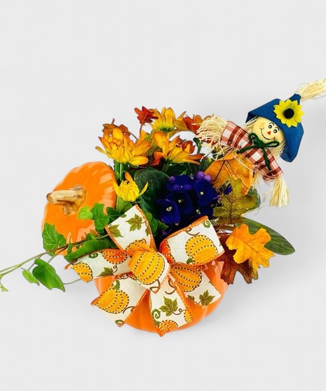 A ceramic pumpkin filled with fall blooming plants accompanied by seasonal textures and a harvest helper.