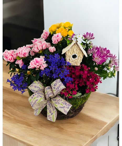 A moss covered basket with pink and white blooming plants and a bird house.