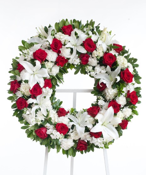 Classic wreath designed with a mix or red roses, white lilies, and other accenting flowers displayed on an easel. Approximate size of the standard design is 18